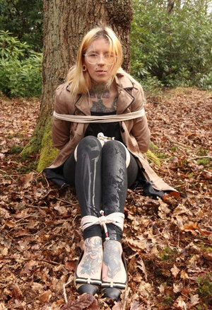 Broad with glasses can't stand up because she is hogtied by the tree