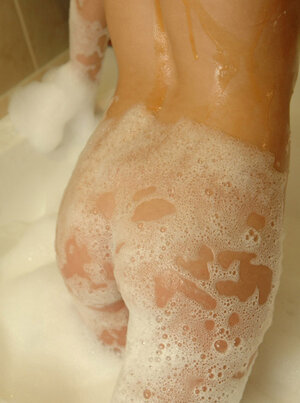 Sweetie takes off green swimsuit and covers the body with foam in the bathtub