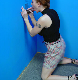 Pretty redhead stands on her knees to blow black fuck pole in a gloryhole room